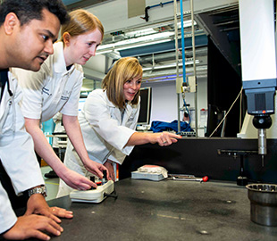 Three people looking at a manufacturing drill machine