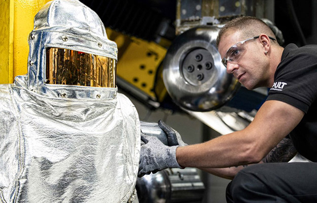 Worker in heat resistant suit and another in a polo shirt and goggles working on machinery